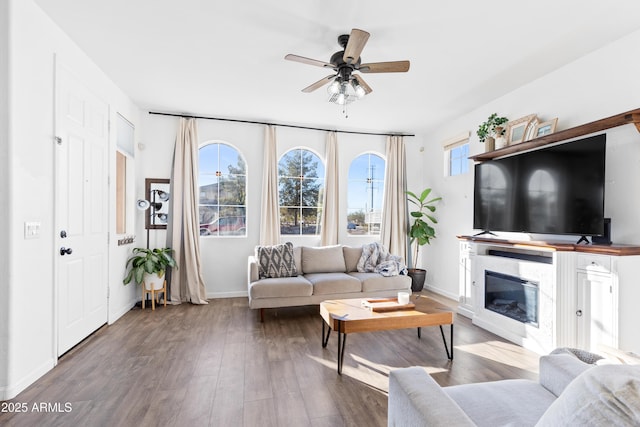 living area featuring a glass covered fireplace, wood finished floors, baseboards, and ceiling fan