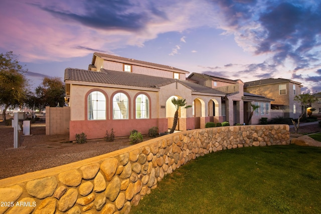 mediterranean / spanish house featuring a front lawn, a tiled roof, fence, and stucco siding