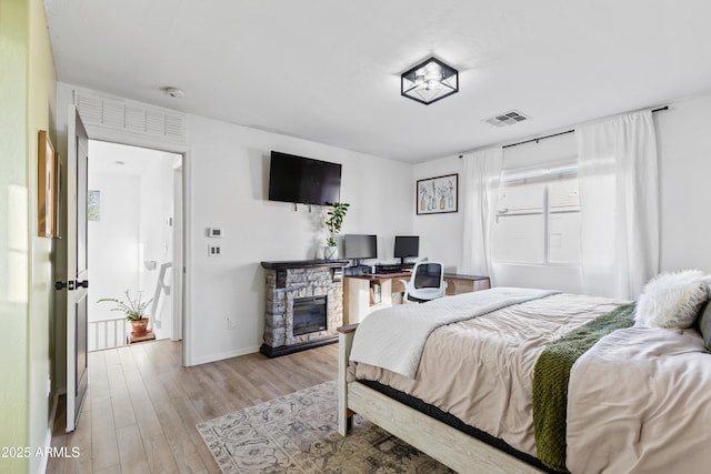 bedroom featuring visible vents, a fireplace, light wood-type flooring, and baseboards