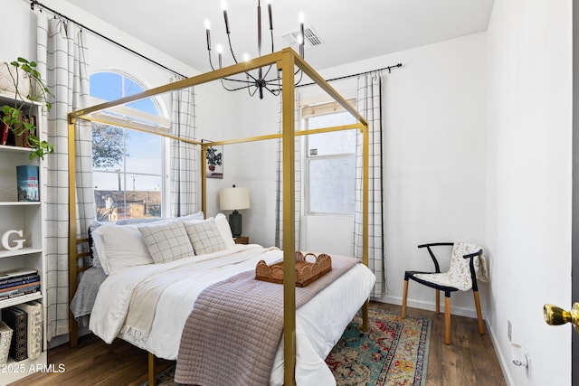 bedroom featuring an inviting chandelier, wood finished floors, visible vents, and baseboards