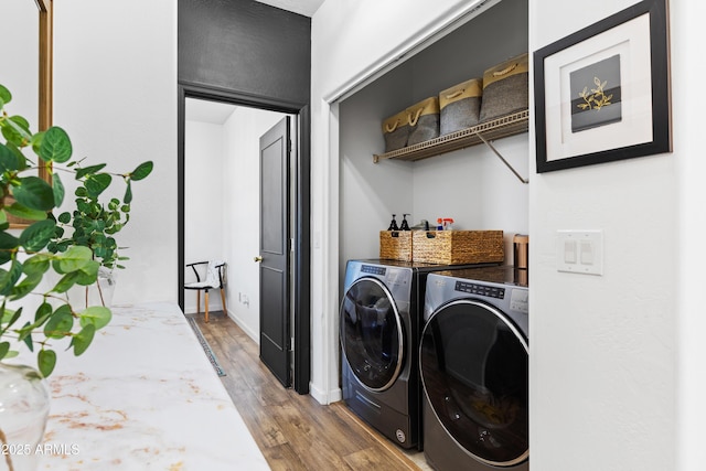 clothes washing area featuring washer and clothes dryer, laundry area, baseboards, and wood finished floors