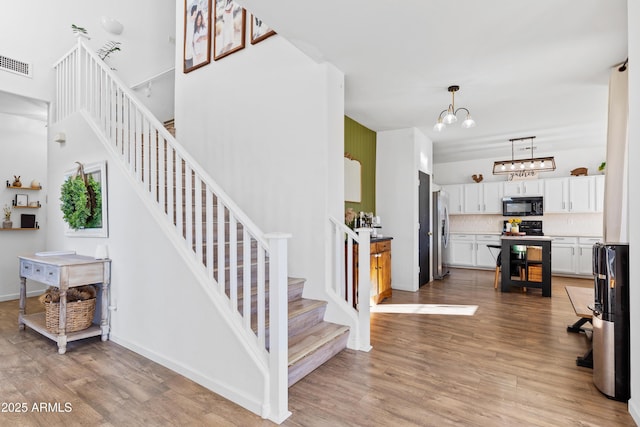 stairs featuring a chandelier, visible vents, baseboards, and wood finished floors