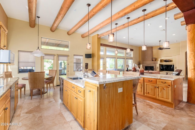 kitchen featuring light stone countertops, beamed ceiling, pendant lighting, a large island with sink, and sink