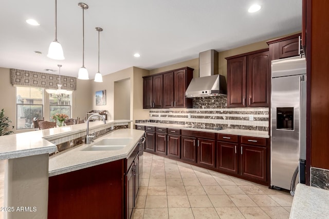 kitchen featuring built in refrigerator, light countertops, decorative backsplash, wall chimney exhaust hood, and a sink