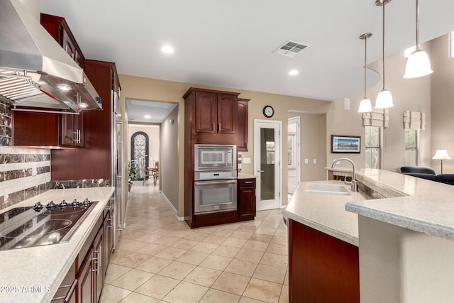 kitchen with visible vents, light countertops, appliances with stainless steel finishes, wall chimney exhaust hood, and a sink