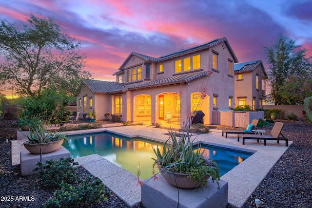 back of house featuring fence, a tile roof, stucco siding, an outdoor pool, and a patio