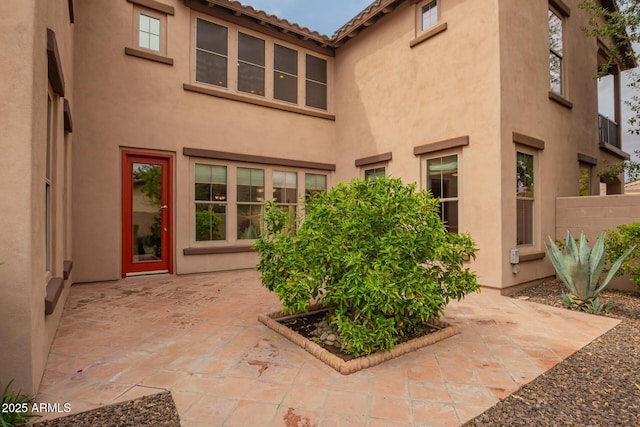 view of exterior entry featuring stucco siding, a patio, and fence