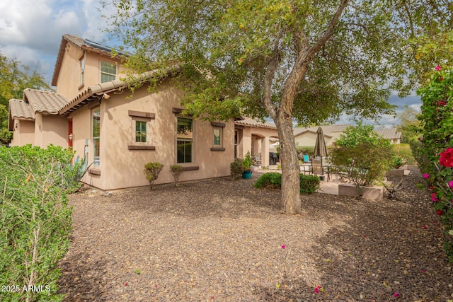 rear view of property featuring a patio, a tile roof, and stucco siding