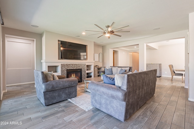 living room with a tile fireplace, light hardwood / wood-style floors, and ceiling fan