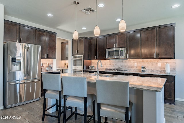 kitchen featuring an island with sink, decorative light fixtures, and stainless steel appliances