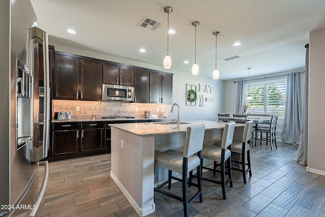 kitchen with a kitchen breakfast bar, hanging light fixtures, stainless steel appliances, light stone counters, and a center island with sink