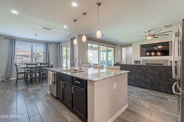 kitchen featuring hanging light fixtures, an island with sink, light wood-type flooring, sink, and light stone counters