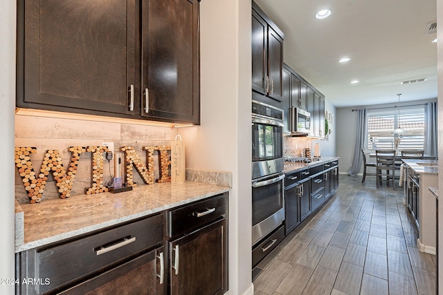 kitchen with light stone counters, appliances with stainless steel finishes, decorative light fixtures, and dark brown cabinets