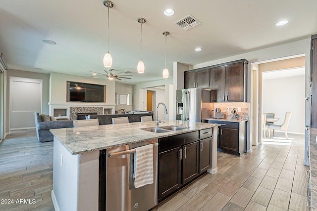 kitchen with dark brown cabinets, sink, light stone countertops, appliances with stainless steel finishes, and ceiling fan