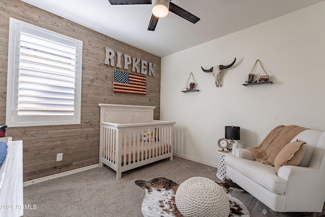 carpeted bedroom with ceiling fan, wood walls, and a nursery area