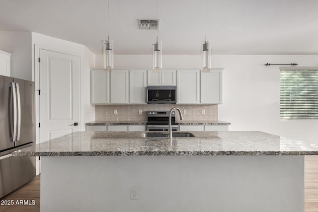 kitchen featuring stainless steel appliances, white cabinetry, a center island with sink, and pendant lighting