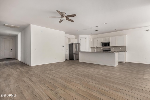 kitchen with stone countertops, appliances with stainless steel finishes, sink, white cabinetry, and a kitchen island with sink