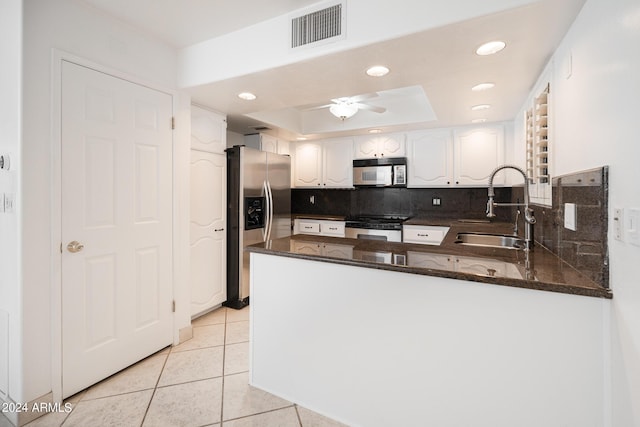 kitchen featuring sink, a raised ceiling, kitchen peninsula, light tile patterned floors, and appliances with stainless steel finishes