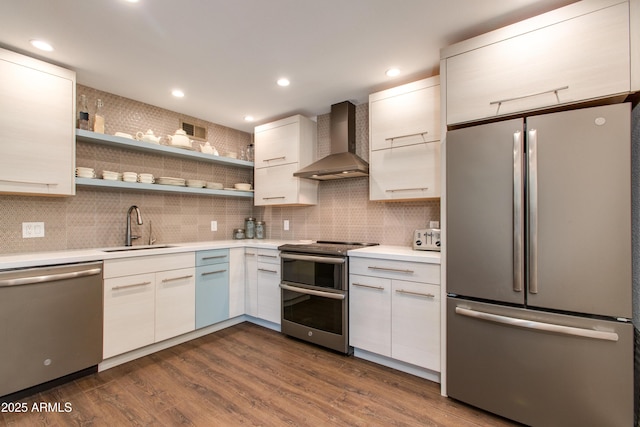 kitchen featuring light countertops, wall chimney exhaust hood, appliances with stainless steel finishes, and a sink