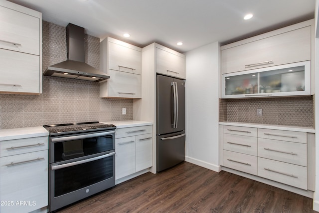 kitchen with dark wood-style flooring, light countertops, appliances with stainless steel finishes, wall chimney range hood, and modern cabinets