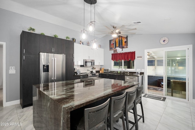 kitchen featuring appliances with stainless steel finishes, ceiling fan, sink, dark stone countertops, and a center island