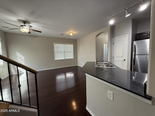 kitchen featuring arched walkways, dark wood finished floors, freestanding refrigerator, a sink, and baseboards