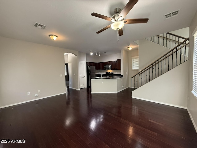 unfurnished living room featuring stairs, visible vents, arched walkways, and dark wood-style flooring