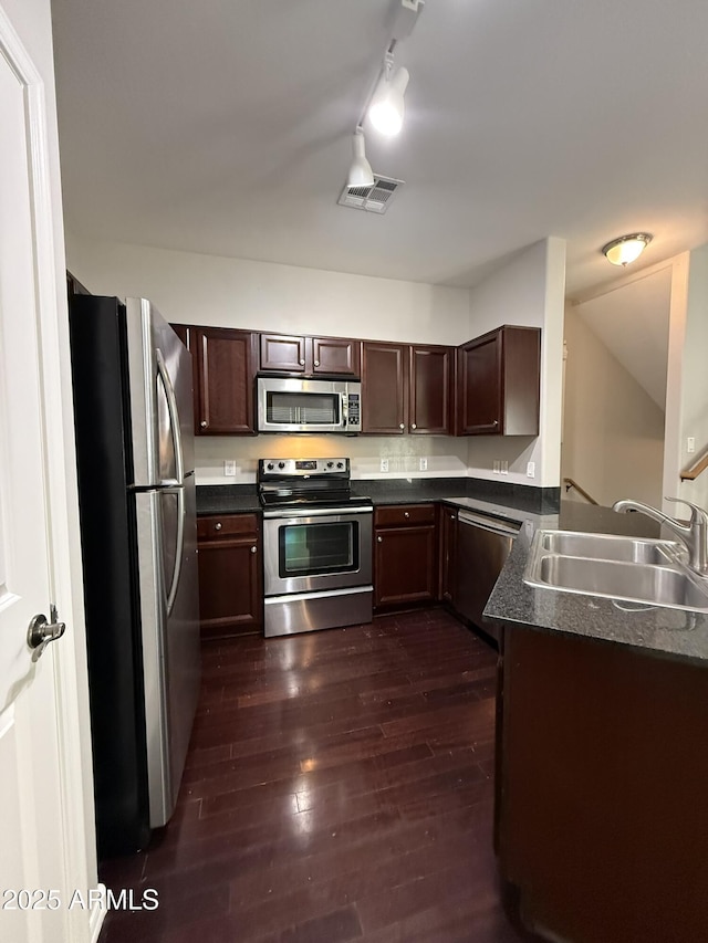 kitchen featuring dark wood finished floors, stainless steel appliances, dark countertops, visible vents, and a sink