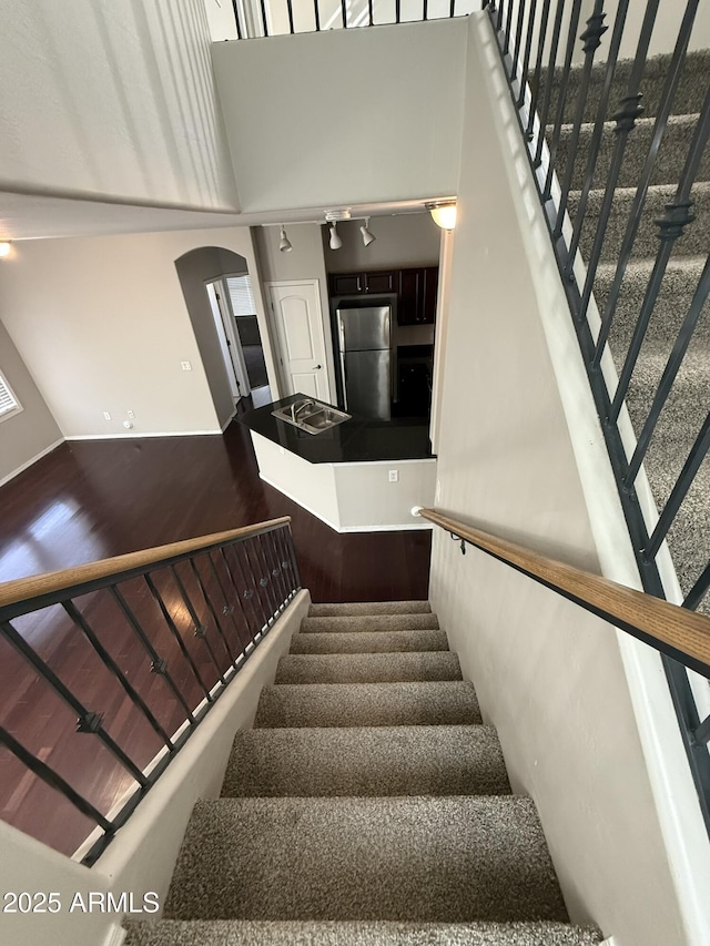 stairs featuring arched walkways, a high ceiling, and wood finished floors