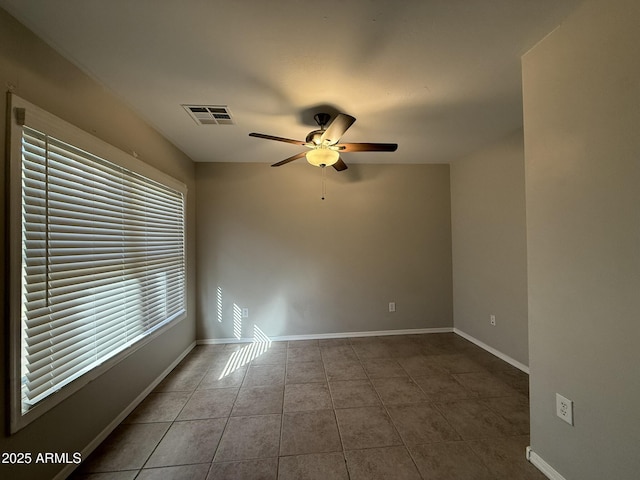 tiled empty room featuring baseboards, visible vents, and a ceiling fan