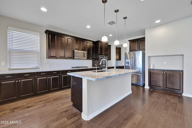 kitchen featuring dark hardwood / wood-style floors, decorative light fixtures, dark brown cabinets, a center island with sink, and appliances with stainless steel finishes