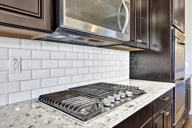 kitchen featuring light stone countertops, backsplash, stainless steel appliances, and dark brown cabinetry