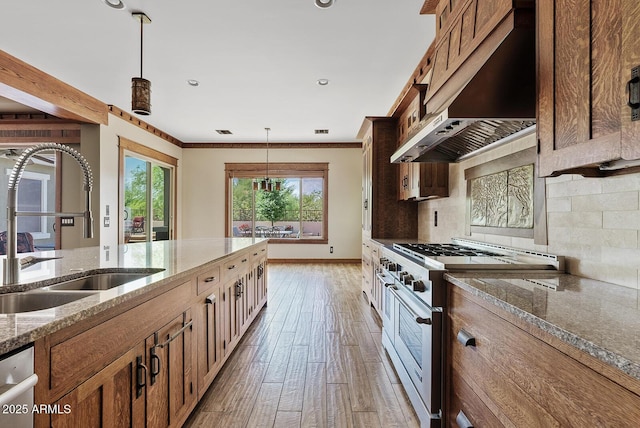 kitchen featuring appliances with stainless steel finishes, a sink, wall chimney range hood, hanging light fixtures, and recessed lighting