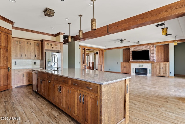 kitchen with stainless steel dishwasher, a sink, a ceiling fan, an island with sink, and light stone countertops