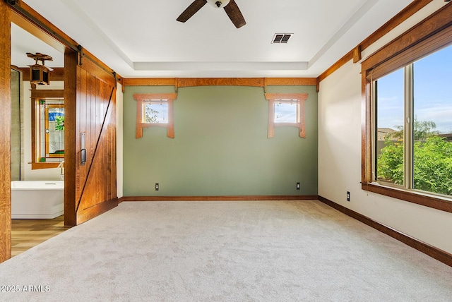 empty room with light colored carpet, healthy amount of natural light, a barn door, and a ceiling fan