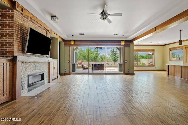 unfurnished living room featuring ceiling fan, a fireplace with flush hearth, wood finished floors, and baseboards