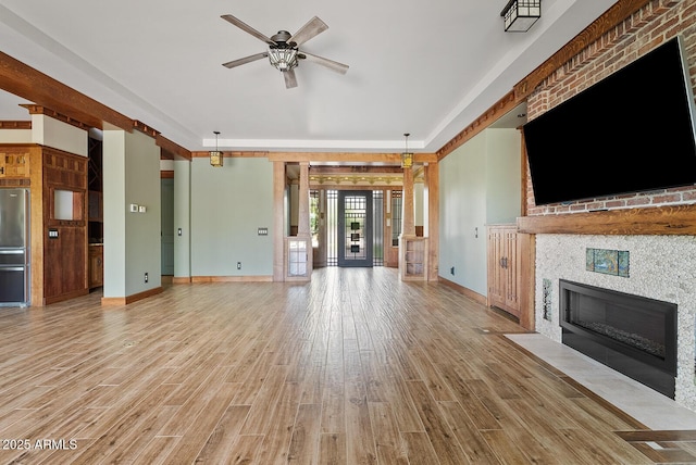 unfurnished living room with a ceiling fan, light wood-style floors, baseboards, and a tile fireplace