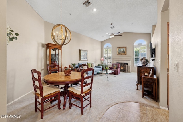 dining space with light colored carpet, lofted ceiling, ceiling fan with notable chandelier, and a tile fireplace