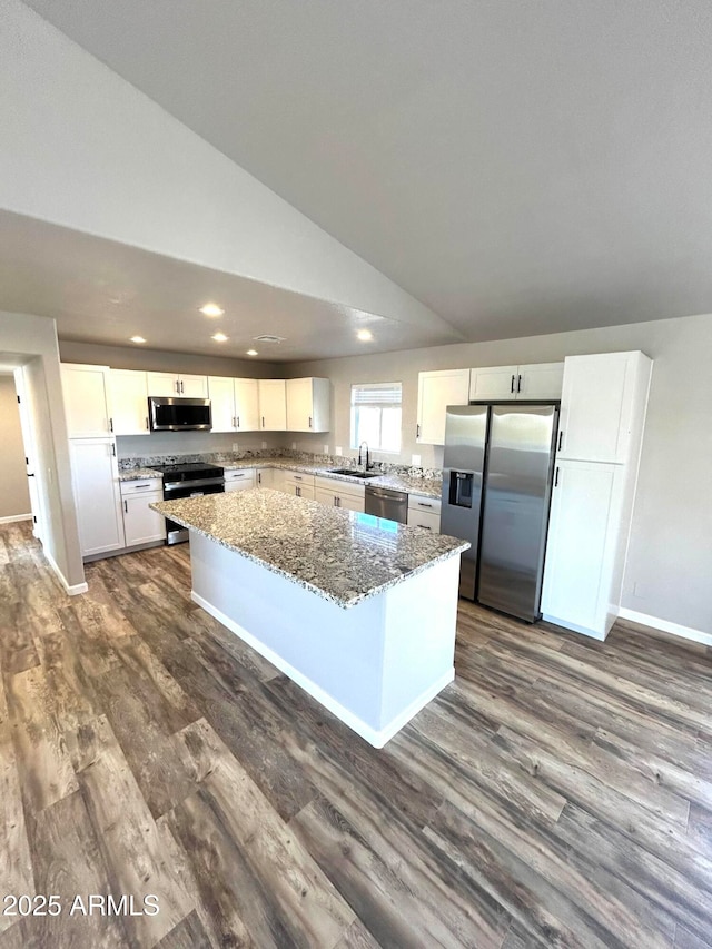 kitchen with appliances with stainless steel finishes, lofted ceiling, a kitchen island, white cabinetry, and light stone counters