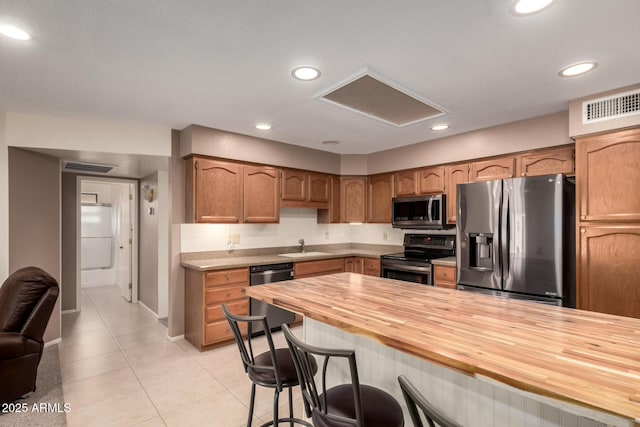kitchen featuring butcher block countertops, a breakfast bar area, recessed lighting, appliances with stainless steel finishes, and light tile patterned floors