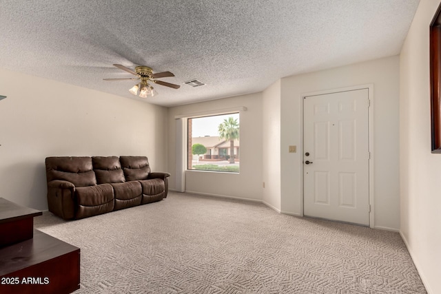 carpeted living room featuring visible vents, a ceiling fan, and a textured ceiling