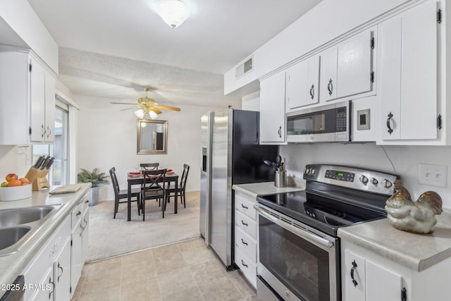 kitchen featuring a textured ceiling, light carpet, appliances with stainless steel finishes, ceiling fan, and white cabinets