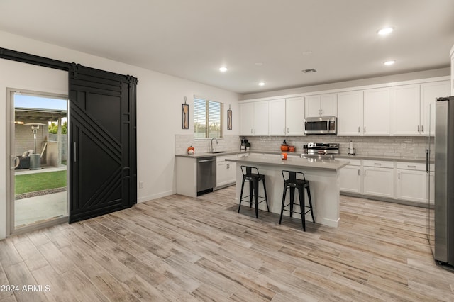 16848 W Alice Ave, Waddell, AZ 85355 - kitchen featuring stainless steel appliances, a sink, backsplash, a barn door, and white cabinetry
