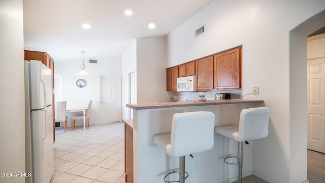 kitchen featuring white appliances, a kitchen bar, light tile patterned floors, hanging light fixtures, and kitchen peninsula