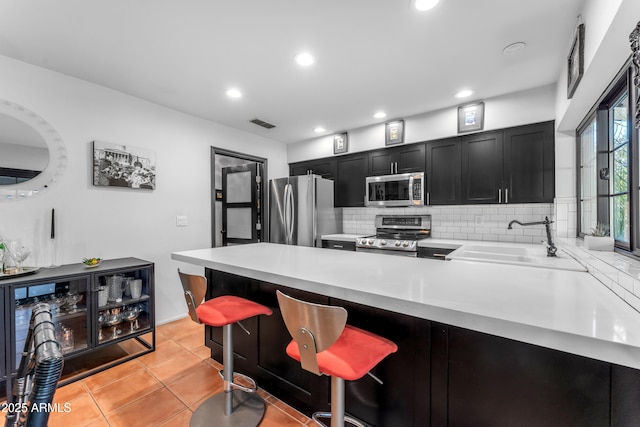 kitchen featuring appliances with stainless steel finishes, a breakfast bar, sink, backsplash, and light tile patterned floors