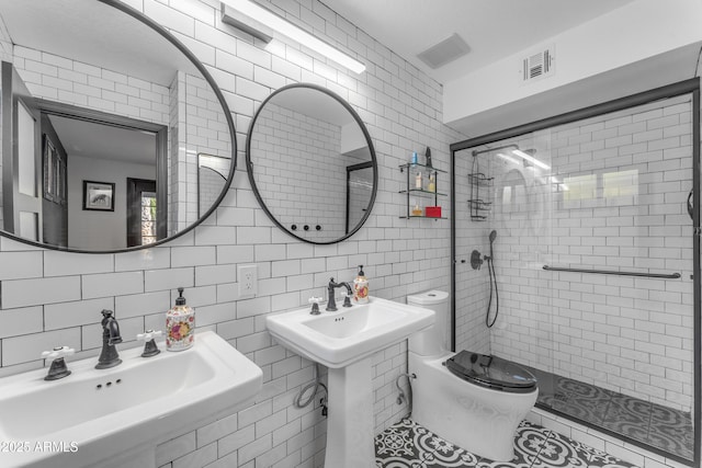 bathroom with tile walls, a tile shower, tasteful backsplash, double sink, and toilet