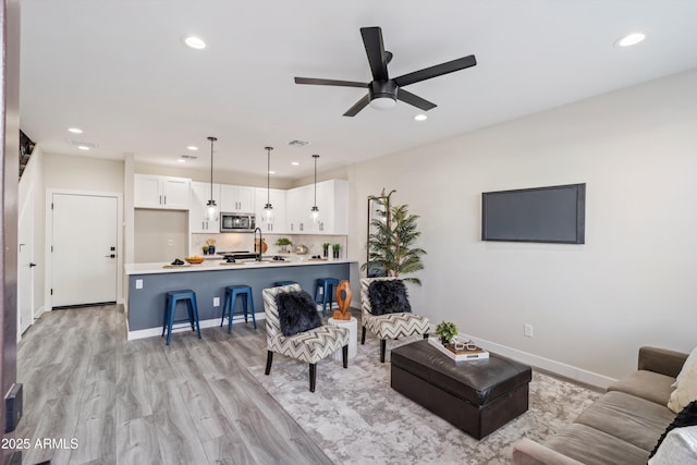 living room with baseboards, ceiling fan, light wood finished floors, and recessed lighting