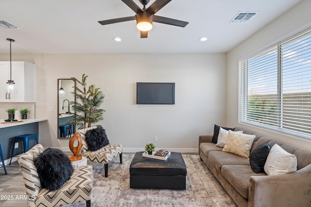 living room with visible vents, light wood-style flooring, baseboards, and ceiling fan
