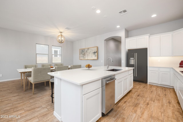 kitchen with high end fridge, sink, white cabinets, a center island with sink, and stainless steel dishwasher