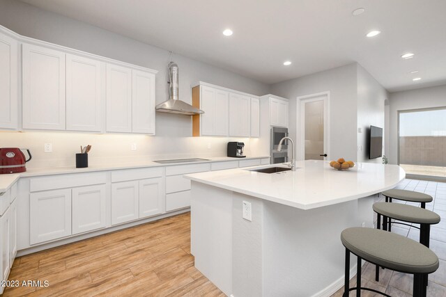 kitchen with sink, light hardwood / wood-style flooring, white cabinets, black electric stovetop, and wall chimney exhaust hood